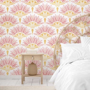 May include: A bedroom with a white wall featuring a pink and yellow geometric pattern wallpaper. A wicker headboard with white bedding is in the foreground. A small wooden side table with a woven basket sits next to the bed.