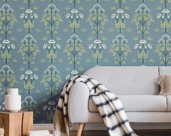 May include: A blue wallpaper with a repeating floral pattern in white and green. A gray sofa with a striped blanket and a decorative pillow is in front of the wallpaper. A white vase sits on a wooden side table.