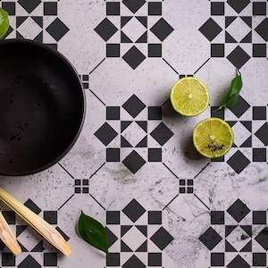 May include: A black bowl, two lime halves, and a stalk of lemongrass on a white and black tiled surface.