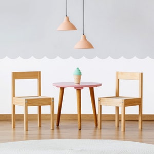 May include: A pink children's table and two wooden chairs with a small ice cream cone decoration on the table.