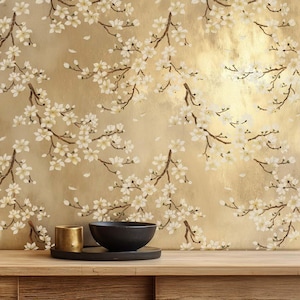 May include: A gold-toned background with a floral pattern of white blossoms and brown branches. A black bowl and a gold-colored cup sit on a wooden surface, adding a touch of contrast to the scene. The overall theme is nature and home decor.
