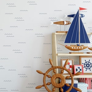 May include: A white wall with a blue wave pattern, a wooden shelf with a blue sailboat, a wooden ship's wheel, and a framed picture with a nautical theme.