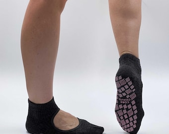 May include: A pair of black grippy socks with a pink "CORE CHAUD" logo on the bottom. The socks have a cut-out for the toes and a strap across the top of the foot.