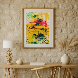 Peut inclure: Un bureau en bois clair avec une chaise assortie et une peinture abstraite encadrée. Une lampe blanche avec un pied en forme de branche et un petit vase sont sur le bureau. La peinture présente des couleurs jaune, verte et bleue.