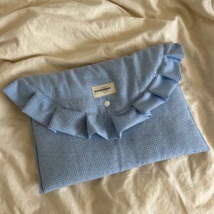 Op de afbeelding: Een blauw en wit geruit kussen van stof met een gerimpelde rand en een witte knoop. Het kussen heeft een label met de tekst "Rosemade" erop.