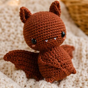 Peut inclure: Une poup&eacute;e chauve-souris faite &agrave; la main, crochet&eacute;e, de couleur marron chaud. La chauve-souris a de grands yeux noirs, de petites dents blanches et des oreilles pointues. Ses ailes sont d&eacute;ploy&eacute;es, et la poup&eacute;e est pos&eacute;e sur une surface textur&eacute;e de couleur cr&egrave;me.