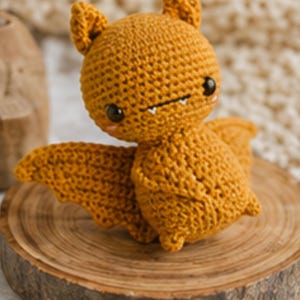 Peut inclure: Une chauve-souris au crochet de couleur orange chaud, avec de grands yeux et de petites dents. Le jouet en peluche fait main a des ailes et des oreilles d&eacute;taill&eacute;es, et est pos&eacute; sur une tranche de bois. Un article charmant et artisanal.