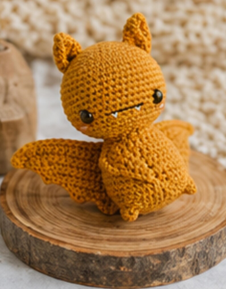 Peut inclure: Une chauve-souris au crochet de couleur orange chaud, avec de grands yeux et de petites dents. Le jouet en peluche fait main a des ailes et des oreilles d&eacute;taill&eacute;es, et est pos&eacute; sur une tranche de bois. Un article charmant et artisanal.