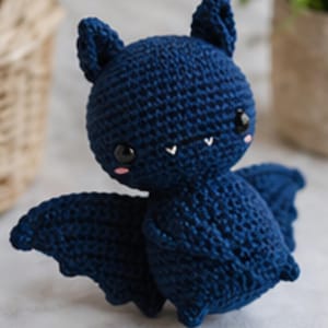 Peut inclure: Une poup&eacute;e chauve-souris au crochet bleu marine, avec des yeux noirs, des joues roses et de petites dents blanches. La chauve-souris a de grandes oreilles pointues et des ailes d&eacute;ploy&eacute;es. Un jouet en peluche fait &agrave; la main.