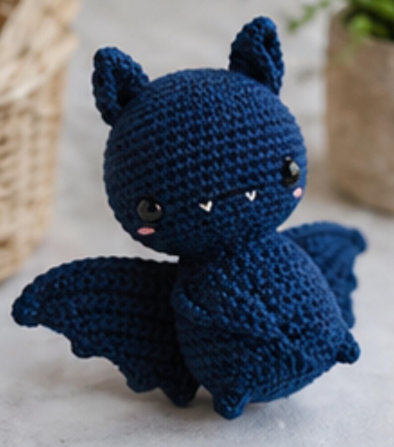 Peut inclure: Une poup&eacute;e chauve-souris au crochet bleu marine, avec des yeux noirs, des joues roses et de petites dents blanches. La chauve-souris a de grandes oreilles pointues et des ailes d&eacute;ploy&eacute;es. Un jouet en peluche fait &agrave; la main.