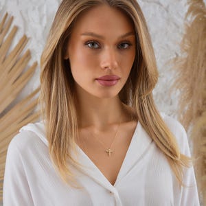 May include: A woman wearing a white shirt with a gold necklace featuring a bee pendant.