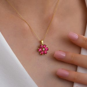 May include: A gold necklace featuring a flower pendant with pink gemstone petals and a small diamond center. The necklace is displayed against a white background.