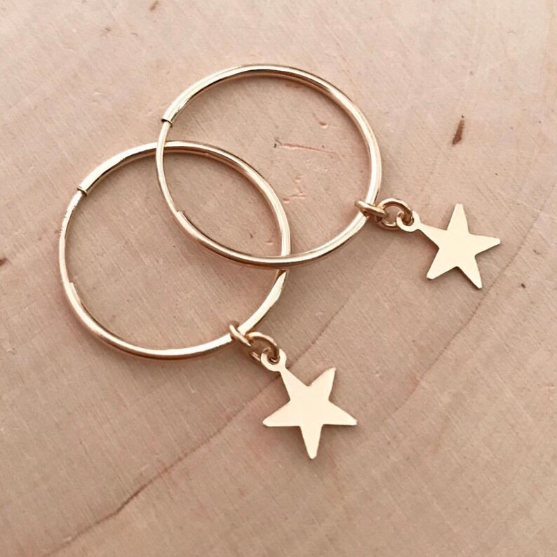 May include: Gold hoop earrings with a small star charm dangling from each hoop.