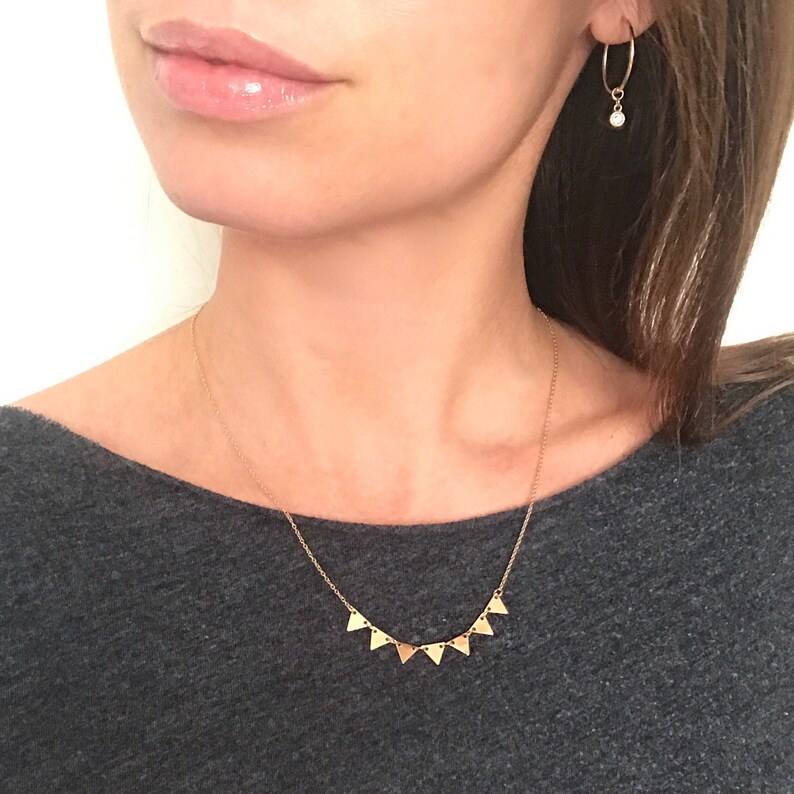 May include: A gold necklace with a delicate chain and a row of small, triangular pendants. The necklace is worn by a person with long brown hair.