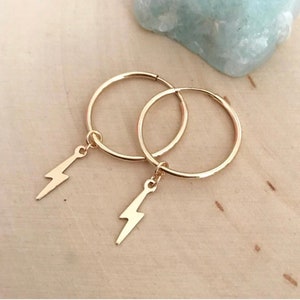 May include: Gold hoop earrings with a small lightning bolt charm hanging from each hoop.