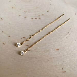 Puede incluir: Un par de pendientes de cadena de oro con una pequeña piedra transparente al final de cada cadena.