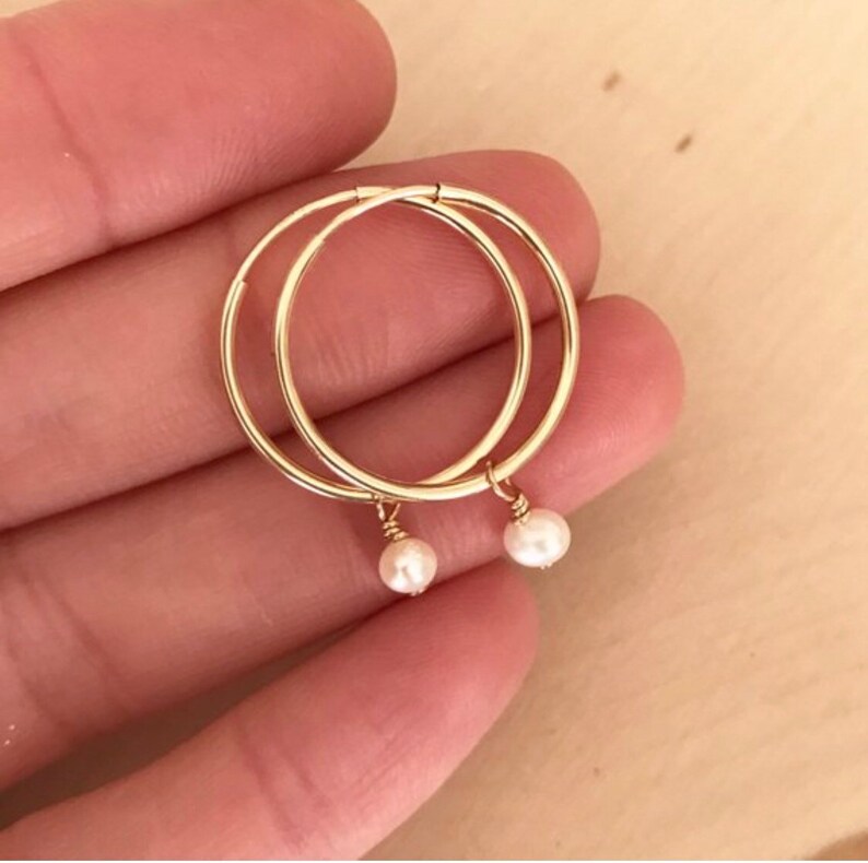 May include: Gold hoop earrings with small pearl charms hanging from them.