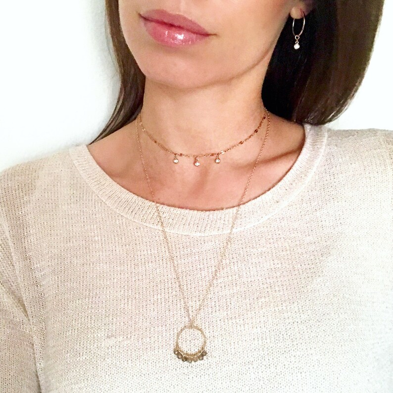 May include: A gold chain necklace with a small circle pendant and a delicate choker necklace with small dangling stones.