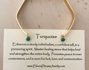 May include: Gold bangle bracelet with turquoise gemstone accents. The card reads "Turquoise" and describes the stone's healing properties and symbolism.  "Enhances a sturdy individualism, a confident will, & a pioneering spirit. Master healing stone that helps heal and strengthen the entire body. Promotes peace & inner contentment, and is worn for luck, love, and communication. www.ElevenDreamsJewelry.com"