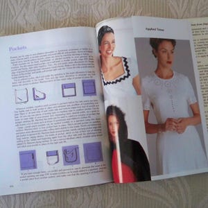 May include: Open book with pages displaying sewing instructions and illustrations. The left page features text about pockets, with diagrams. The right page shows a photo of a white dress with decorative trim. A woman in a white top is also visible.