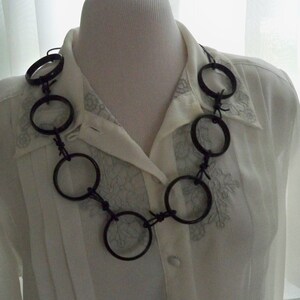 May include: A black necklace made of large, round, metal rings connected by barbed wire.