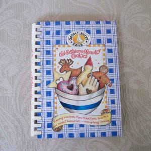 May include: A spiral-bound cookbook titled "Old-Fashioned Country Cookies" with a blue and white checkered cover. The cover illustration features a bowl overflowing with various cookie shapes, including stars, hearts, and gingerbread figures. The Gooseberry Patch logo is at the top.