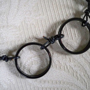 May include: A black leather necklace with two black, round, polished metal rings connected by the leather cord. The rings are interlocked.
