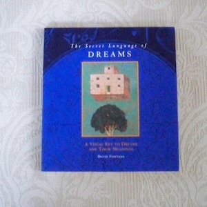 May include: A book titled "The Secret Language of Dreams" with a blue cover. The cover features an illustration of a floating building above a tree. The text "A Visual Key to Dreams and Their Meanings" and the author's name are also visible.