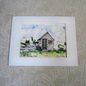 May include: Watercolor painting of a weathered wooden shack on a shoreline, under a blue sky with birds. The artwork is framed in white, with the text "Appledore, N.H. Fisherman's Shack" and the artist's signature.