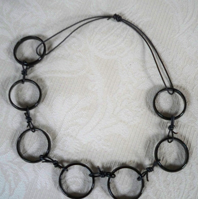 May include: A black necklace made of metal rings connected by black string. The necklace has a simple design and is made of multiple rings.