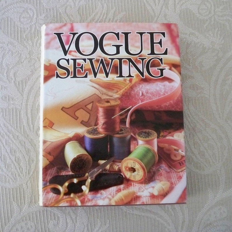 May include: A book titled "VOGUE SEWING" with a colorful cover featuring spools of thread, scissors, and sewing notions. The cover has a pink and beige background with the title in large black letters.