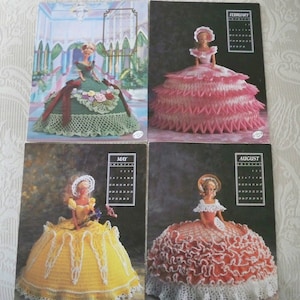 May include: Four crocheted doll dresses in different colors, each with a doll head and a calendar page for a different month. The dresses are green, pink, yellow, and red.