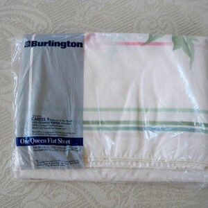 May include: A white queen-sized flat sheet in a plastic bag. The sheet has green and red stripes and is labeled "CARESS II Natural for the Touch 80% CELANESE FORTREL 20% Combed Cotton/Cotton" and "One Queen Flat Sheet".