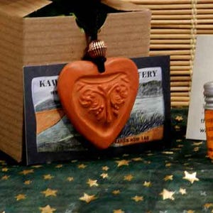 May include: Aromatherapy set for car, closet, or drawer. The set includes a small glass bottle with a silver cap, a heart-shaped orange pendant, and a cardboard box. The text on the card reads "AROMATHERAPY for CAR, CLOSET or DRAWER".