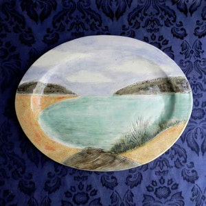 May include: A ceramic oval serving platter featuring a painted scene of a bay with a sandy beach and green grass. The sky is painted in shades of blue and white.
