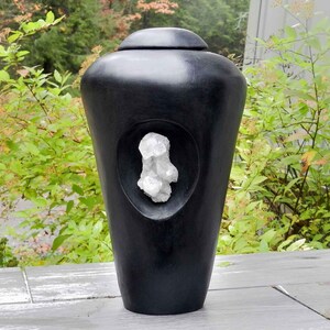 May include: A black urn with a white crystal embedded in the front. The urn is made of wood and has a smooth, polished finish.