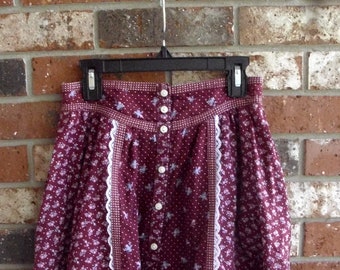 May include: A burgundy skirt with a white lace trim and a floral print. The skirt has a button-up front and a tiered ruffle hem.