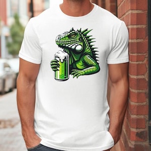 Puede incluir: Camiseta blanca con una iguana verde sosteniendo una jarra de cerveza verde.