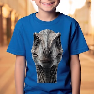 Może przedstawiać: Niebieska koszulka z zbliżeniem twarzy velociraptora.