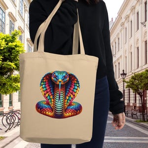 Könnte beinhalten: Eine beige Tragetasche mit einem bunten Schlangendesign. Die Schlange ist in einer gewickelten Position mit erhobenem Kopf und herausgestreckter Zunge. Die Schlange besteht aus einer Vielzahl von Farben, darunter Rot, Orange, Gelb, Grün, Blau und Lila.