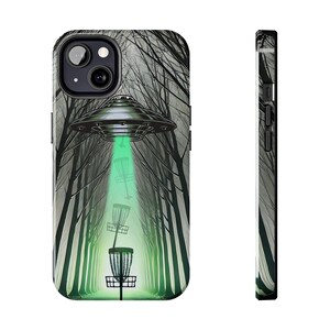 May include: A phone case featuring a surreal scene of a UFO beaming a green light onto disc golf baskets in a forest. The case has a black border and a glossy finish, perfect for protecting your phone.