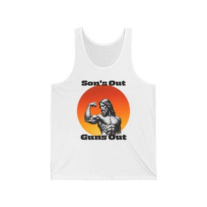 Peut inclure: Un débardeur blanc avec un graphique d'une figure musclée avec un soleil éclatant derrière. Le texte "Son's Out Guns Out" est imprimé sur le t-shirt.