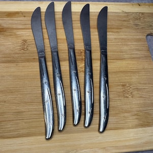 Puede incluir: Juego de cinco cuchillos de cena de acero inoxidable plateado con diseños en forma de estrella en los mangos.
