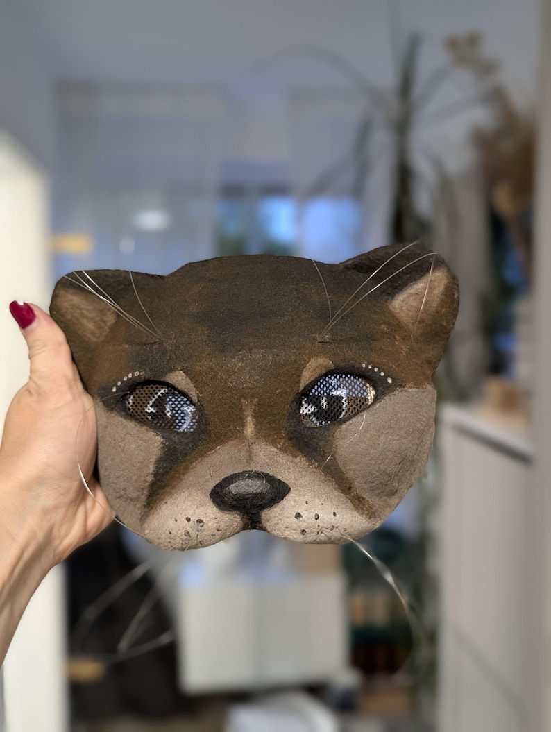 May include: A brown cat mask with detailed facial features, including mesh eyes and whiskers. The mask is hand-painted with a realistic design, showcasing a playful and artistic aesthetic. This unique mask is suitable for costume parties or theatrical performances.
