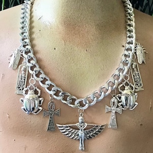 May include: Silver-toned chain necklace with various Egyptian-themed charms. The necklace features a large curb chain and pendants including scarab beetles, ankh crosses, and a winged goddess. The necklace is displayed on a mannequin.