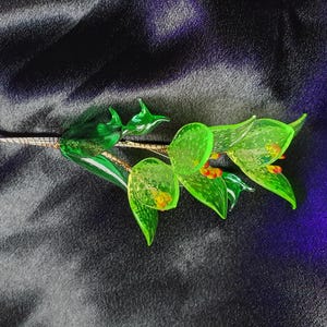 May include: A glass flower bouquet with green leaves and orange accents. The bouquet is made of glass and has a delicate, whimsical look.