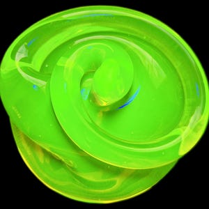 Puede incluir: Un diseño abstracto y arremolinado en verde brillante, sobre un fondo negro. La superficie brillante refleja la luz, creando reflejos y sombras. La forma se asemeja a una flor estilizada o una forma orgánica. Se ven toques de azul y amarillo.