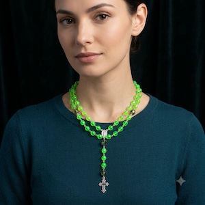 May include: A double-strand rosary necklace featuring vibrant lime green translucent beads, interspersed with darker olive-toned beads. The necklace includes a central silver-toned metal medal and a matching silver-toned crucifix pendant at the base.