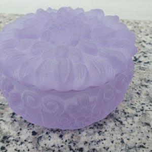Peut inclure: Une boîte à bijoux en verre lavande avec un motif floral. Le couvercle présente un motif de fleur en relief et la base a un motif floral tourbillonnant.