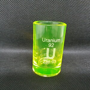 May include: A neon green shot glass with the text "Uranium 92 U 238.03" printed on the side.